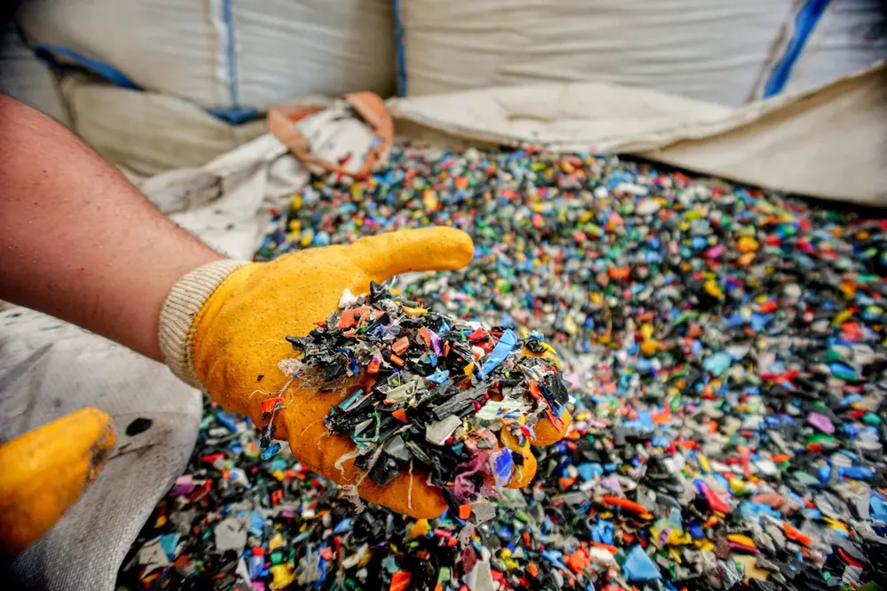 Shredded plastic flake held in a gloved hand, the condition most material arrives in